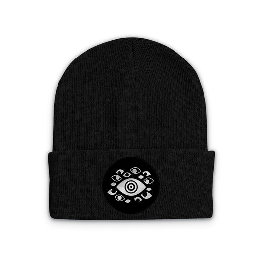 Black beanie with a circular emblem in the center of the cuff featuring silver eyes.