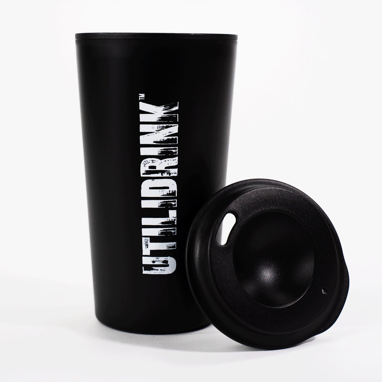 Photo of a black drink tumbler with a plastic lid. On the side it says, “UTILIDRINK” in white distressed lettering. 