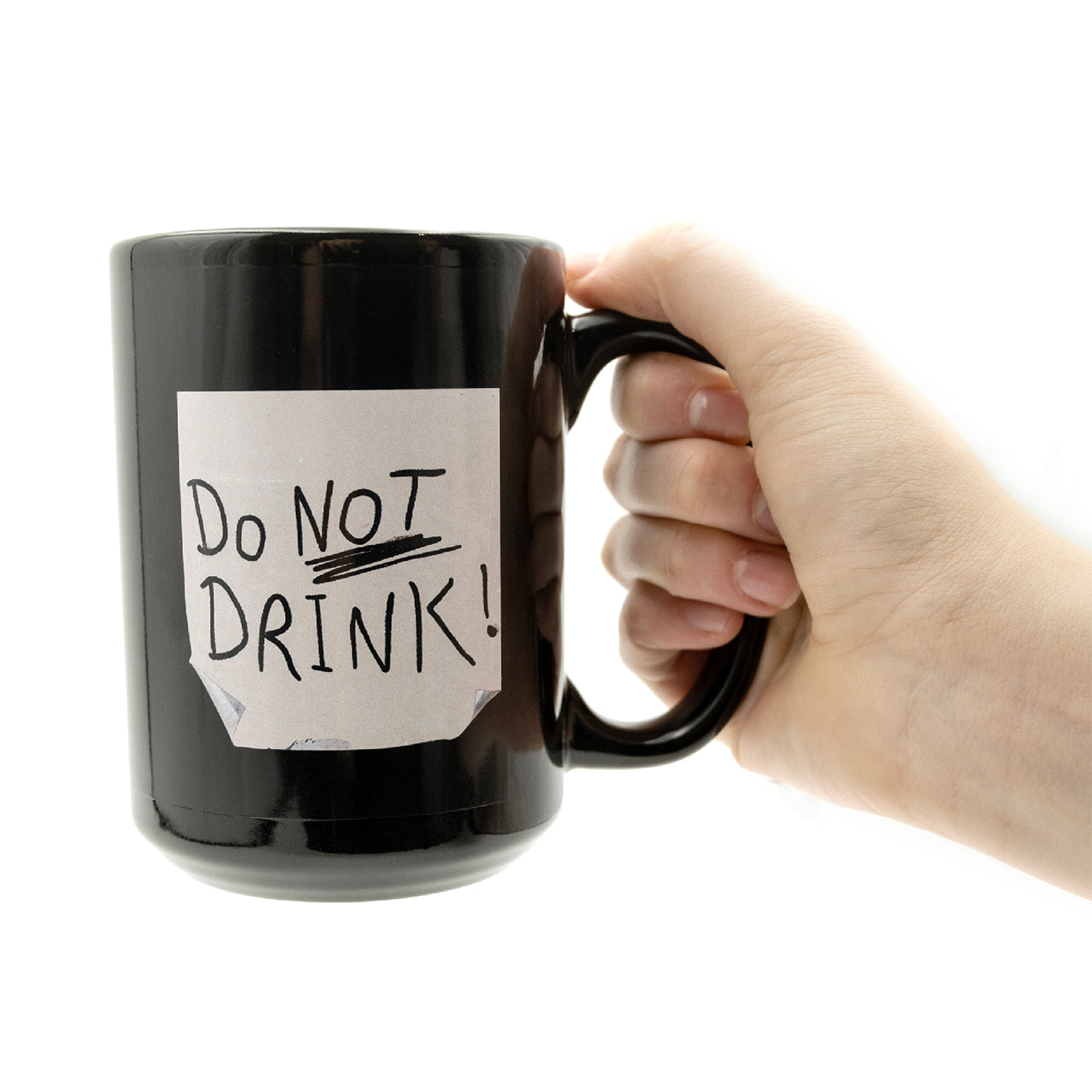 15 oz black mug with a print to look like a distressed post it note with the text DO NOT DRINK scribbled on it in black marker with its handle being held by a hand.