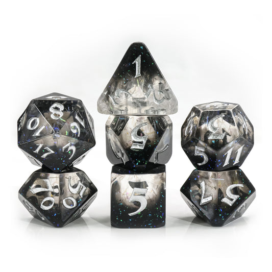 Image of a set of polyhedral dice. They are cast in clear and black resin with iridescent glitter flakes. The numbers are painted silver.