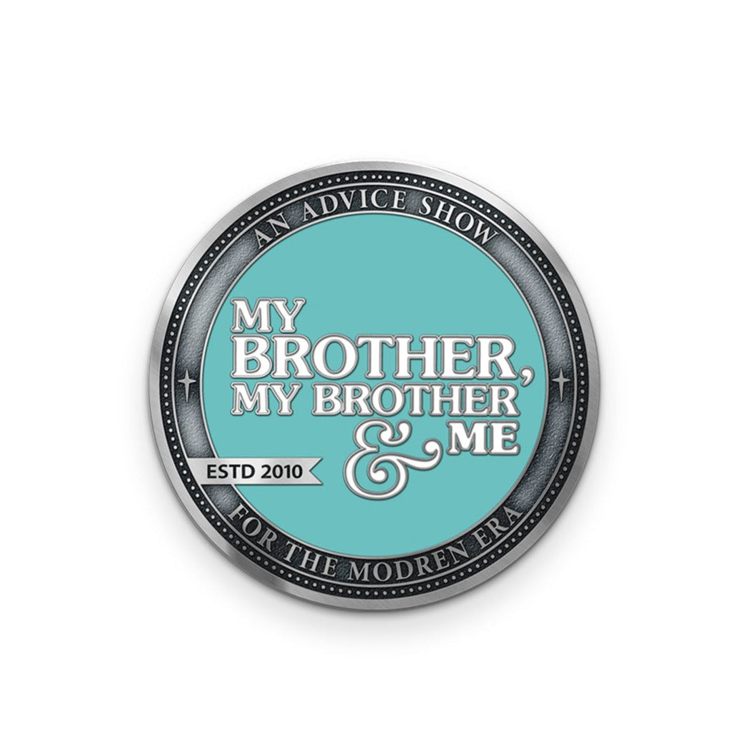 A silver coin with a teal center that says, "My Brother, My Brother & Me" in white. Around it is a border that says "An advice show for the modren era" with a silver banner that says "ESTD 2010". There is a border around that of dots.