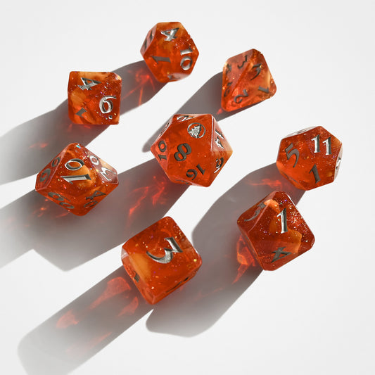 Image of an orange dice set with silver lettering. The dice have yellow veins and glitter running through the center of them. The 20 on the D20 is a silver pine tree in a circle. 