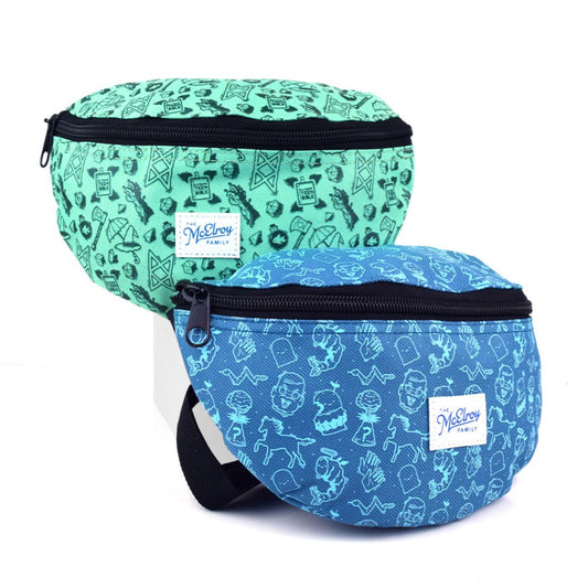 Image of two fanny packs. One is teal with dark green illustrations and the other is blue with light blue illustrations. Both have a white patch that says, "The McElroy Family" in blue font. Both have black zippers. The teal fanny pack has drawings of the B.o.B. sigil, the extreme teen bible, Merle's arm, Magnus's ax, Taako's umbrella and hat, and a d20. The blue fanny pack has illustrations of a doll head, an angular snake, a shrimp with wings and halo, two hands waving, a ghost, and a horse.