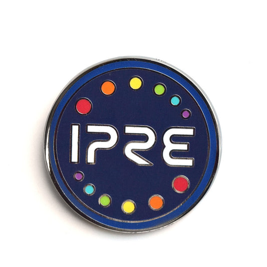 A circular dark blue enamel pin. In the center it says, "IPRE" in white. Above and below that are twelve rainbow dots. There is a light blue border.