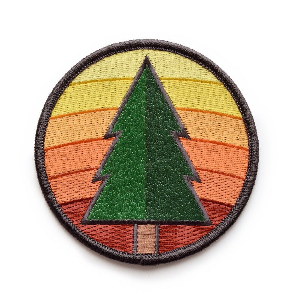 A circular patch The background is a yellow to orange gradient. On top of that is a light and dark green pinetree with a brown trunk. 