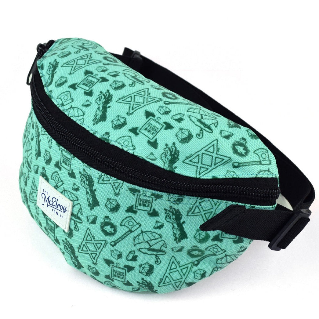 A teal fanny pack covered in dark green illustrations with a white patch that says, "The McElroy Family" in blue. There are drawings of Merle's arm, the B.o.B. sigil, the Extreme Teen Bible, Magnus's ax, Taako's umbrella and hat, a d20, a crystal, and Stephen the fish in his bowl.